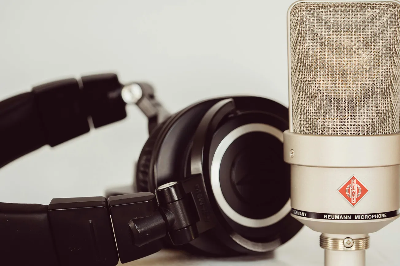 Close-up of a professional microphone and black over-ear headphones against a neutral background.